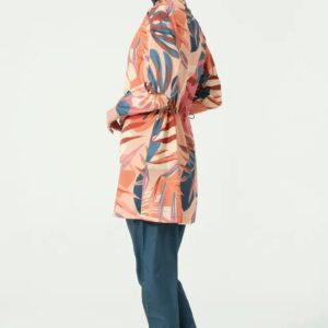 Woman wearing a tropical coral burkini set with a colorful leaf-patterned top and plain navy blue pants, styled with a matching navy swim cap, posing side view against a white background.